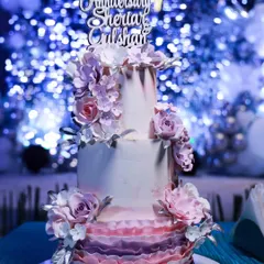 A slightly different angle of the lavender ombre 25th-anniversary cake, highlighting the texture of the ruffles and the arrangement of the sugar flowers.
