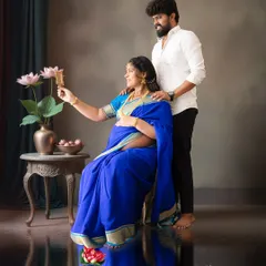 A creative maternity portrait where the expectant mother, dressed in a vibrant blue saree, looks at her reflection in a traditional 'aranmula kannadi' mirror held by her partner.