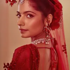 The quintessential red bride, looking over her shoulder. The makeup is classic and clean, with a defined eye and balanced lip, allowing the stunning red outfit and jewelry to shine.