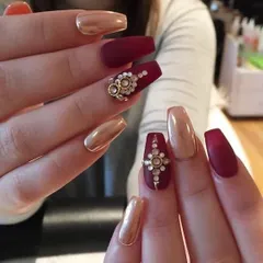 An example of intricate 3D bridal nail art. This design pairs matte maroon and chrome gold nails with a stunning, hand-crafted floral embellishment made from gold and pearl-like gems.