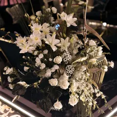 A close-up of a floral arrangement for "The Dark Club" theme. The composition of white blooms and dark, sculptural leaves provides a soft yet dramatic contrast against the moody decor.
