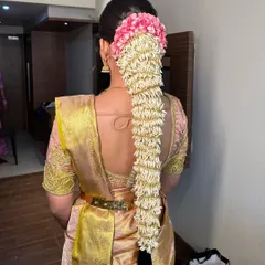 A traditional South Indian bridal hairstyle featuring a long braid fully covered in fresh jasmine flowers (gajra), with a touch of pink flowers at the top. This is a classic and fragrant choice for a wedding.