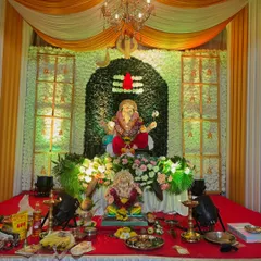 A beautiful home Ganpati decoration featuring a floral wall in the shape of a Shivling. This setup combines fresh flowers, elegant drapes, and a chandelier to create a divine and welcoming space for Bappa.
