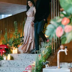 A couple makes a grand entrance down a staircase adorned with tropical florals and quirky mushroom props for their 'Citrus Safari' themed reception. We love creating immersive experiences that transport your guests.