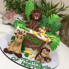 A cute jungle-themed cake to celebrate six months of happiness. This ganache cake features adorable, handcrafted fondant animals like a lion, giraffe, and monkey, surrounded by tropical leaves and bananas.