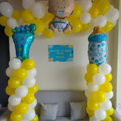 A sweet 'Welcome to Nani House' setup for a baby boy. It includes yellow and white balloon pillars, baby-themed foil balloons, and a personalized welcome sign.