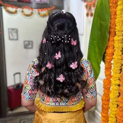 A whimsical and creative hairstyle for a Haldi ceremony. This half-up style features a delicate bow made of hair and is decorated with playful butterfly clips and pearls for a fun, youthful vibe.