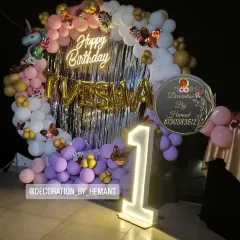 A magical unicorn theme for a first birthday party. This setup features a circular backdrop with a silver fringe, a custom neon "Happy Birthday" sign, foil letters for the name, and a large light-up number '1' to mark the special milestone.