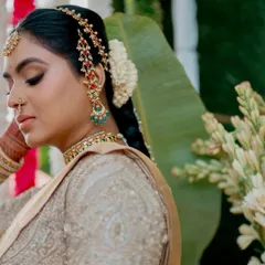 A close-up of a bride's profile, highlighting her traditional hairstyle and jewelry. Her golden silk saree and matching embroidered blouse were custom-designed to create a look of timeless elegance.