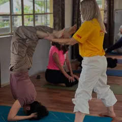 An instructor provides crucial support to a student working on her Scorpion Pose. This hands-on assistance is key to understanding the alignment and balance required for inversions.