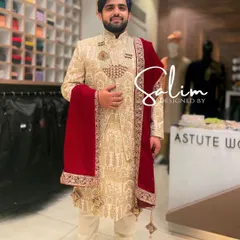 A classic groom's look featuring an ivory sherwani with dense, tonal embroidery. I've paired it with a rich, red velvet stole that has a detailed gold embroidered border, adding a touch of color and luxury.