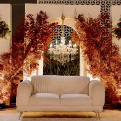The reception stage, where a simple white sofa is set against a backdrop of arched panels, crystal chandeliers, and dramatic bursts of red foliage, creating a look of modern romance.