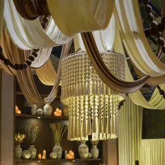 The ceiling is a masterpiece of texture, with flowing drapes in earthy tones and a magnificent tassel chandelier. The beaded garlands add another layer of rustic detail to the design.