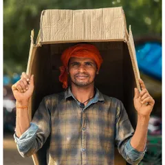 A candid portrait of a worker in Delhi, who playfully uses a cardboard box for shelter from the sun. His direct gaze and smile tell a story of making the best of any situation.