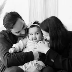 An intimate black and white portrait showing a mother, father, and baby sharing a close, loving moment.