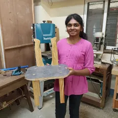 A student holding a unique chair she designed, featuring wavy backrests. Our workshops encourage creativity and out-of-the-box thinking.