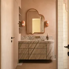 We call this bathroom a 'chic desert dream'. It features blush-toned micro-concrete walls and a monolithic vanity carved from veined Corteccia marble. The stone appears to trickle down onto the floor, creating a fluted skirting detail that is both organic and luxurious.