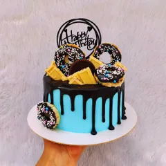 A fun drip cake topped with mini donuts, white chocolate bars, and Oreos. The bright blue buttercream provides a great pop of color.