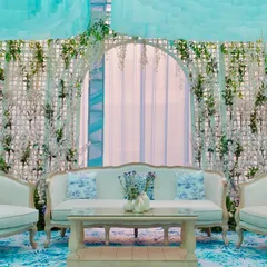 A chic seating area designed for a couture Mehendi. The lounge features elegant French-style furniture, custom-printed cushions, and a backdrop of white trellises with delicate floral arrangements.