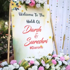 A personalized welcome sign for the Haldi ceremony of Darsh and Sureshi. The sign is beautifully decorated with floral arrangements, setting a warm and welcoming tone for the event.