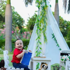 A happy one-year-old boy enjoys an outdoor picnic-themed shoot, laughing as he plays with a book in the fresh air.
