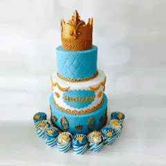 A royal-themed cake fit for a prince's celebration. This three-tiered masterpiece features quilted patterns, gold accents, and a crown topper, complete with matching cupcakes for the guests.