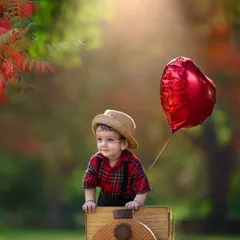 All aboard for a happy birthday ride. This toddler portrait uses a toy train prop and a heart-shaped balloon to create a sweet and celebratory scene in a beautiful, naturally lit park.