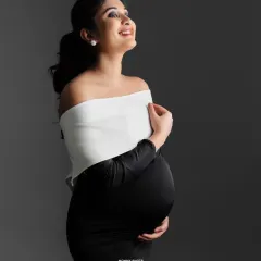 A joyful, radiant maternity portrait in a classic black and white gown against a simple grey backdrop.