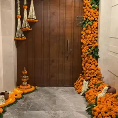 I make your home's entrance feel truly festive and welcoming. This traditional doorway decoration features dense garlands of fresh orange marigolds, accented with hanging jasmine tassels and a floral rangoli, setting a perfect tone for any celebration like Diwali or a housewarming pooja.