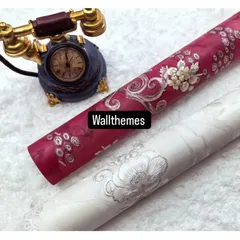 Two wallpaper rolls with a classic floral damask design, one in deep magenta and one in off-white, both with silver accents.
