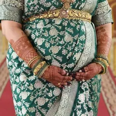 A close-up shot focusing on the baby bump and the beautifully stained mehendi. The deep reddish-brown color of the henna looks stunning against her traditional green and silver saree.