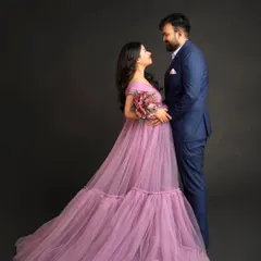 A romantic studio portrait of an expecting couple. The partner's formal suit complements the elegance of the lavender maternity gown, creating a timeless and classic image.