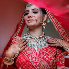 A close-up of the bride adjusting her stunning emerald and polki necklace, with the veil softly framing her face. This shot focuses on the luxurious bridal jewelry.