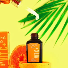 A single drop of Lakme Vitamin C serum is captured mid-air, demonstrating the product's lightweight feel while the vibrant orange background reinforces its core ingredient.