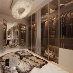 A view of a luxurious walk-in closet, where mirrored finishes, soft lighting, and curated detail are at every glance. The space includes glass-fronted wardrobes, a central island with a tufted ottoman, and a statement chandelier, celebrating the private joy of dressing up.