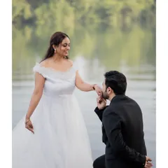 The groom-to-be kisses his fiancée's hand during their pre-wedding shoot by the water, a classic romantic gesture captured in beautiful natural light.