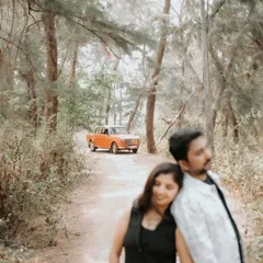 A quiet, romantic moment between the couple, with the vintage car in the background setting a nostalgic scene in the woods.