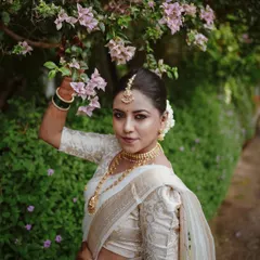 A beautiful outdoor bridal portrait, with the bride posing under a bougainvillea tree, perfectly complementing her white and gold saree.