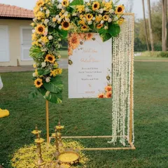 For this outdoor Haldi ceremony, we created a welcoming entrance that blends modern design with tradition. The custom sign is framed by an arc of fresh sunflowers and delicate jasmine strings, with brass lamps adding a customary touch.
