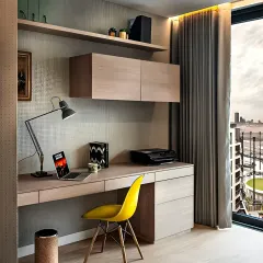 This minimalist home office setup features a light wood desk with slim drawers and matching floating shelves and cabinets. The large window provides plenty of natural light for a productive environment.