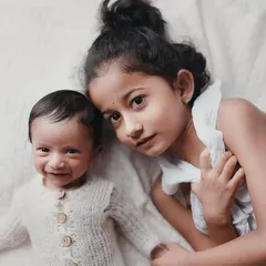 A close-up portrait of an older sister and her smiling newborn brother. This image is filled with so much tenderness and love.