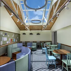 A closer look at the transformed attic space, where modern lighting and flexible furniture meet the original wooden ceiling structure. This adaptive reuse project focuses on creating comfortable and sustainable environments that bring nature and light indoors.