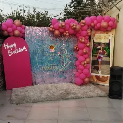 A glamorous birthday photo booth with a pink sequin wall that shimmers in the light. The setup is completed with a pink balloon arch, a custom "Happy Birthday" sign, and a personalized photo standee.