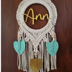 This macrame name hanging for 'Ann' combines natural cotton with pops of teal and mustard yellow leaves. It's a perfect, customized gifting option for a loved one.