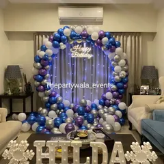 A beautiful balloon ring in blue, purple, and silver, set up in a living room. The fairy lights woven into the balloons and the light-up name sign create a magical, frozen-like effect.