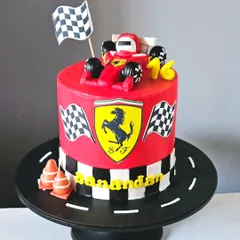 A sleek Ferrari-themed cake for a racing fan. This cake is covered in red-colored ganache and features the iconic Ferrari logo, a checkered flag pattern, and a handcrafted Formula 1 car topper.