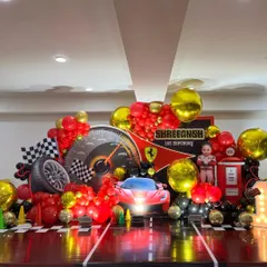 This is a full stage setup for a Ferrari car racing theme. It features a personalized backdrop, 3D car and gas pump props, and a dynamic balloon arrangement in signature red, black, and gold.