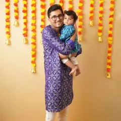 A father and son in matching traditional kurtas pose for a photo during their family's Ganesh Chaturthi celebration. This is a wonderful way to capture cultural traditions.