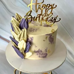 A striking birthday cake with abstract, sculpted chocolate shards in shades of lilac and white. The design is finished with a modern palette knife texture and flecks of gold leaf.