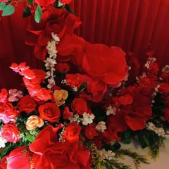 A close-up of the floral arrangement, showing a mix of real and high-quality artificial red roses and paper flowers. This combination adds texture and volume to the engagement decor.